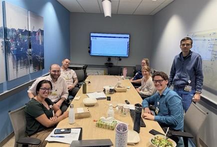 Seven hematology fellows sit around a table discussing patient cases.