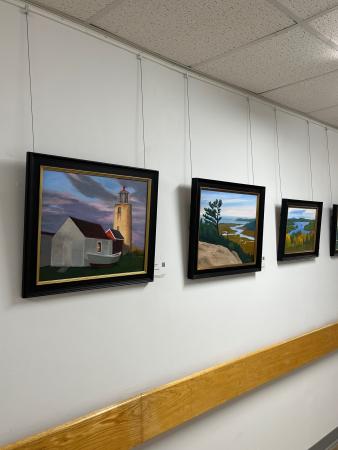 Collection of brightly-colored landscape paintings in black frames handing on a wall in a hallway
