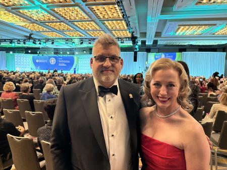 Devin Carr and Valerie Fuller dressed formally and standing together at an awards ceremony in a large room full of people
