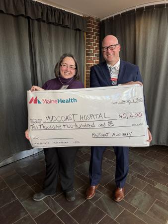 A man and a woman standing together and smiling while holding a large display check for a donation presentation