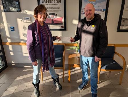 A man and a woman standing together and smiling with a check as part of a donation presentation