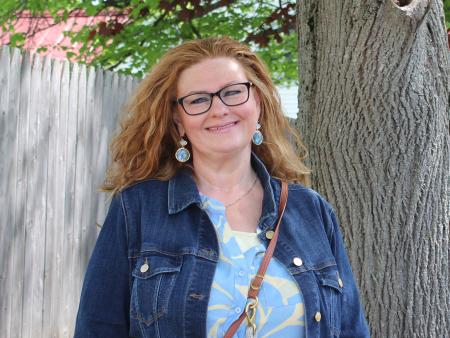 Erika, a residential care worker, smiling and standing outside next to a tree on a sunny day