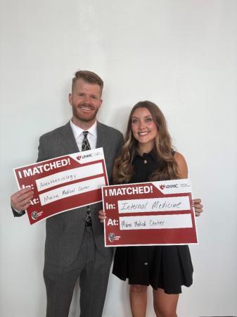 a man and a woman standing together and smiling, holding signs that say "I matched". The man's sign indicates he's matched to Anesthesiology and MHMMC and the woman's sign indicates she's matched to internal medicine at MHMMC 