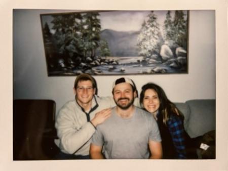 two men and a woman sitting together on a couch and smiling