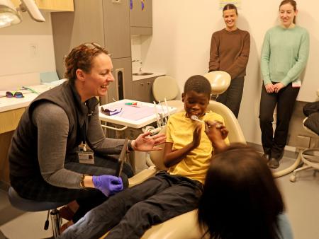 A young boy receives a dental exam in a dentist office while two care team members observe