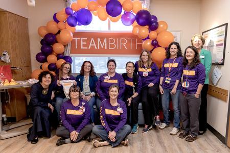 A group of care team members posing together in front of a large balloon arch and banner that says "teambirth"