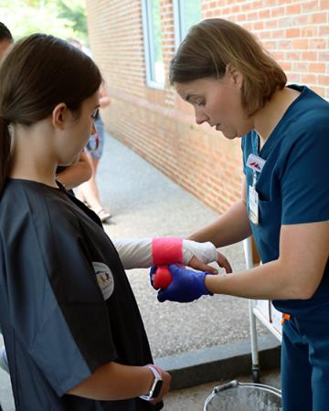 A care team members demonstrates applying medical tape on student's arm