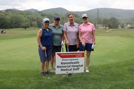 four adults, members of team barker, posing together on the greens during the Memorial Hospital golf tournament