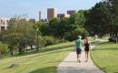 Two people walk on a path surrounded by green grass and trees. Maine Medical Center is seen in the distance.