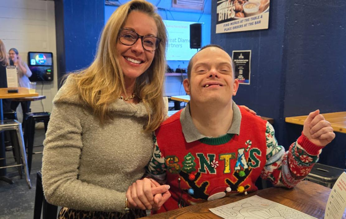 A smiling woman holds hands with a young man wearing a holiday sweater