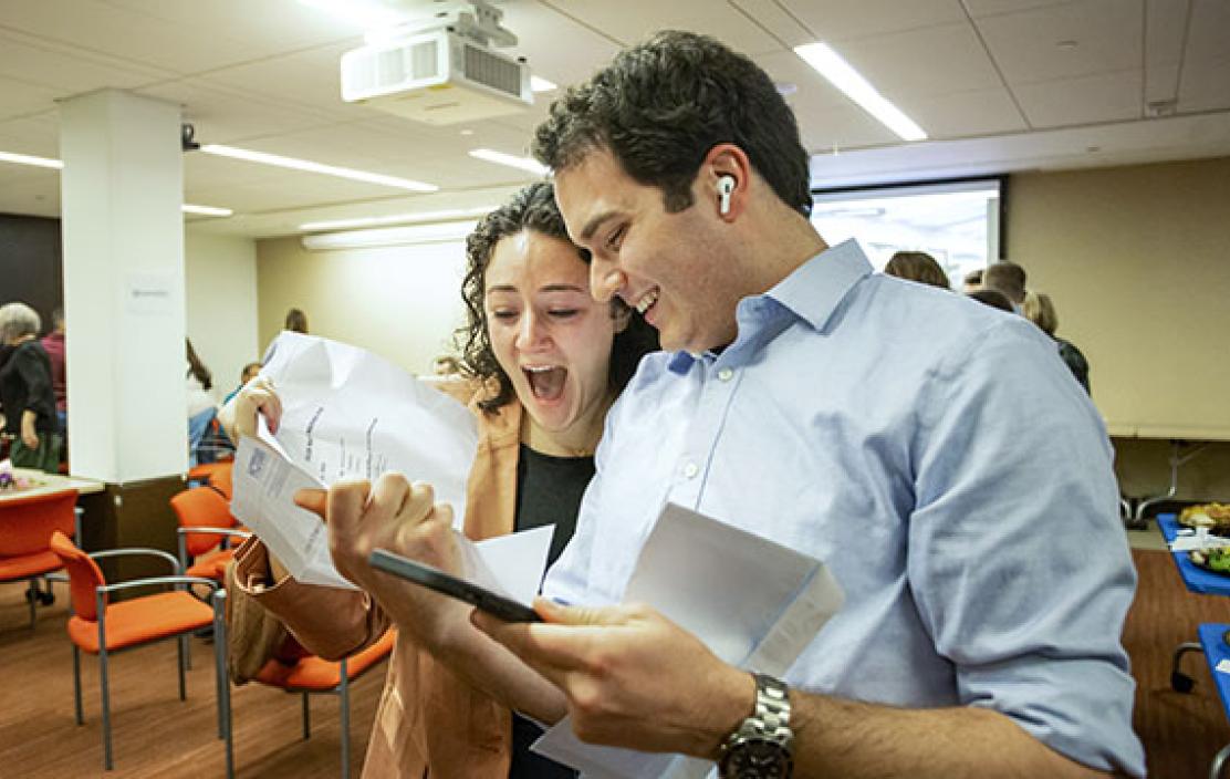 a young man and a woman celebrate together while looking at a sheet of paper