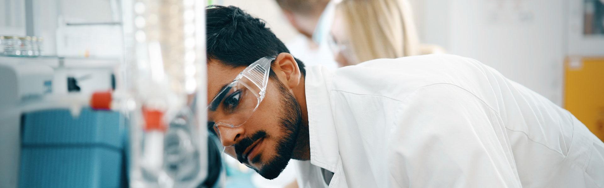 A male lab tech monitors a test with co-workers behind him