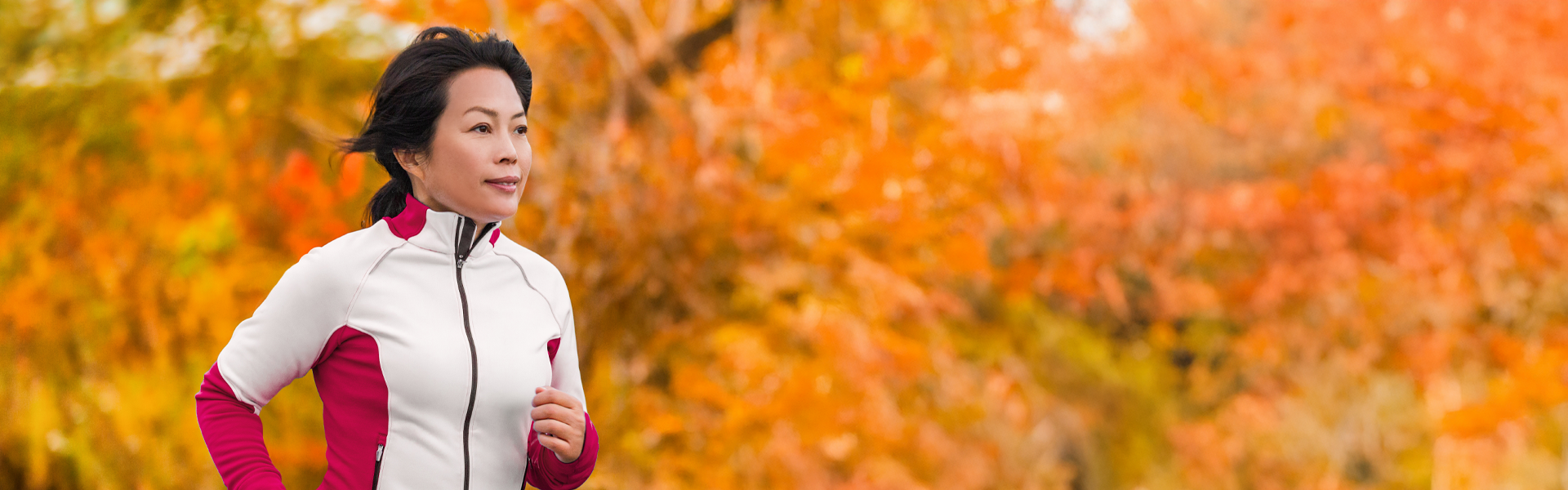 A woman is running through a wooded area with bright orange foliage