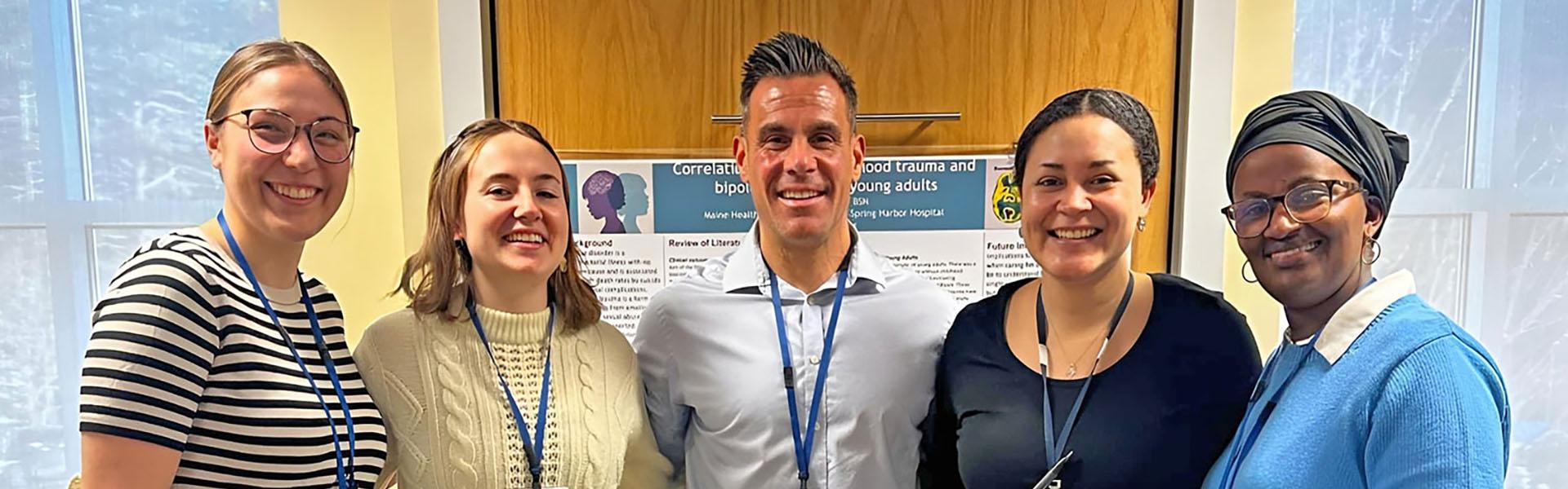 Graduates Mediatrice Kantarama, RN; Toia Francis, RN; Shane Grenier, RN; Delaney Collins, RN; Samantha Holichork, RN standing together in front of large windows