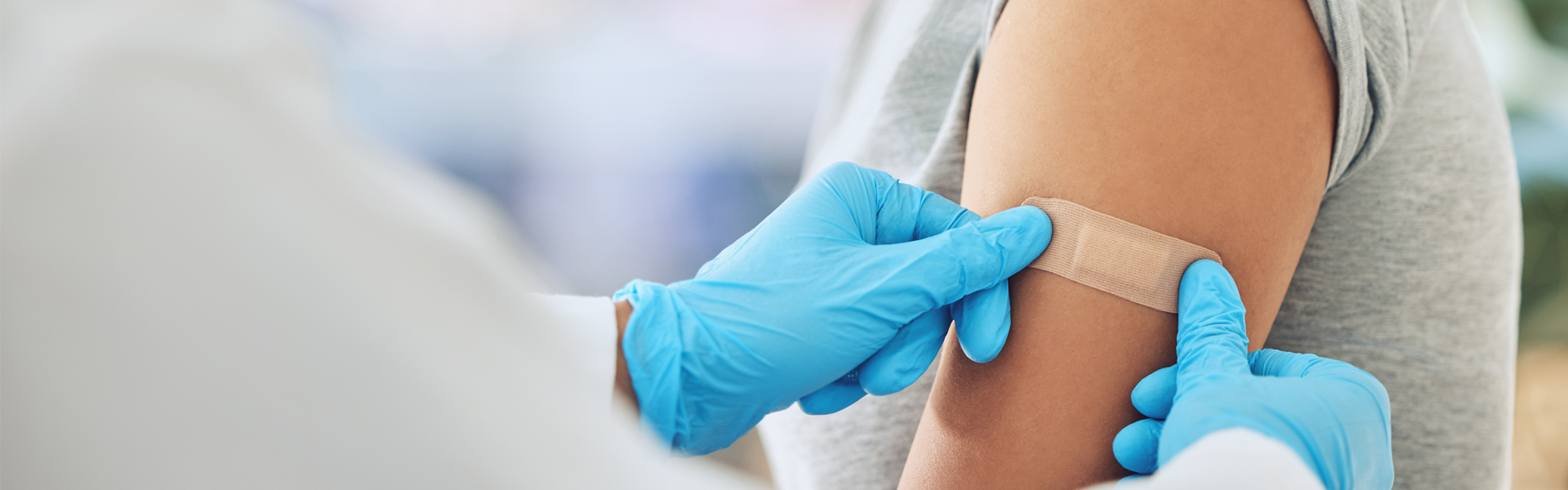 Two gloved hands applying a bandage to a patient's arm following a vaccination