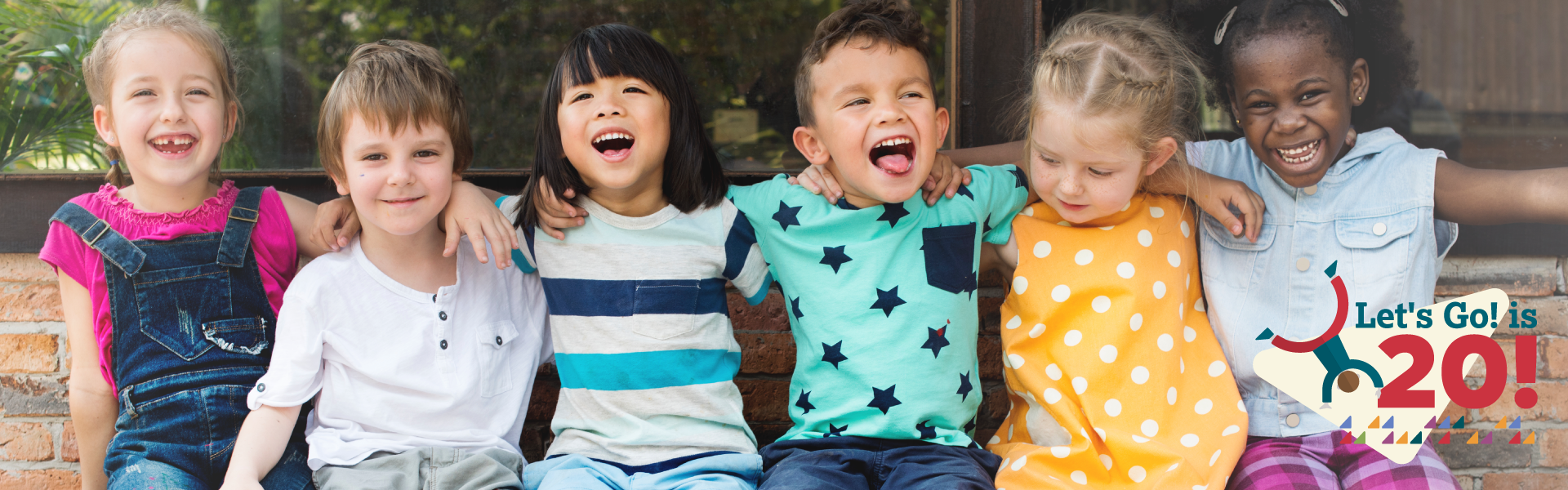 A group of five children sit together outside with their arms around each other's shoulders