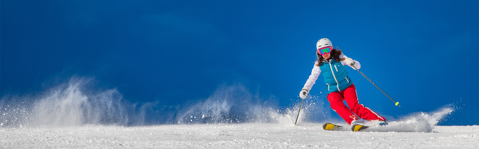 A person wearing brightly-colored ski gear while skiing down a mountain. It is a bright day with a blue sky.