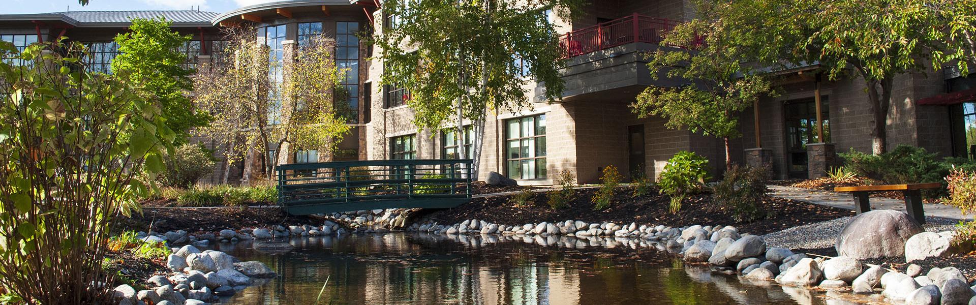 The healing garden at MaineHealth Franklin Hospital with ample trees and foliage, a calm pond, and benches