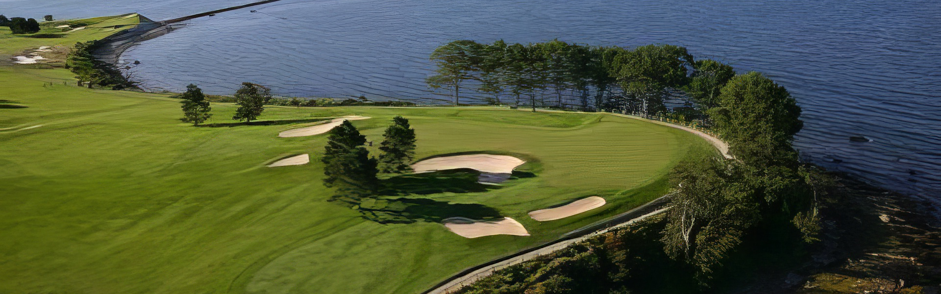 View of a golf greens and hole on a lush course next to the ocean from far overhead