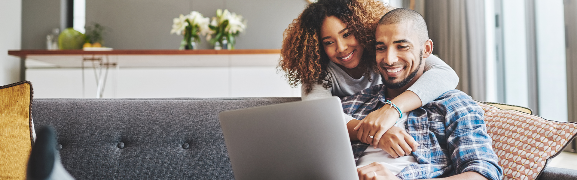 A couple embrace on a couch while looking at a computer screen