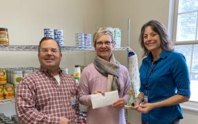 Three adults standing together in front of metal kitchen shelves stocked with dry goods