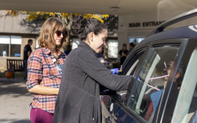 Two care team members administer a flu vaccine to a person through their car window at drive-thru vaccine clinic