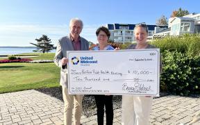 Three adults standing together holding an over-sized check for a grant award presentation