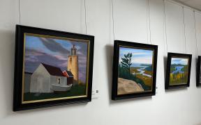 Collection of brightly-colored landscape paintings in black frames handing on a wall in a hallway