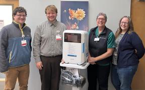 four care team member standing in a hospital hallway with a new, portable, disinfection device