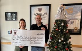 A man and a woman standing together holding an over-sized check for a donation presentation