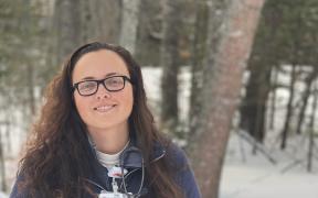 Megan Harvey standing outside in the snow in front of the woods