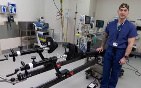 Dr. Zethariah Zielinski wearing scubs and standing next to a specialized orthopedic surgical table in an operating room