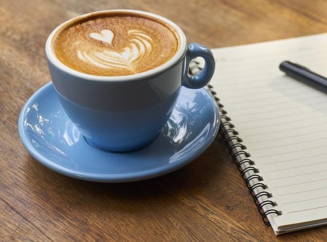 A full cup of coffee sits on a table next to a notebook and pen