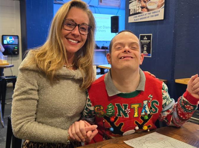 A smiling woman holds hands with a young man wearing a holiday sweater