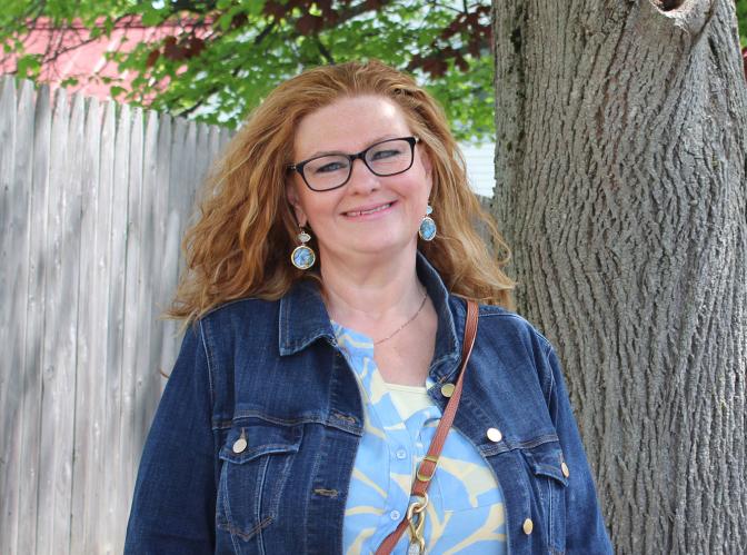 Erika, a residential care worker, smiling and standing outside next to a tree on a sunny day