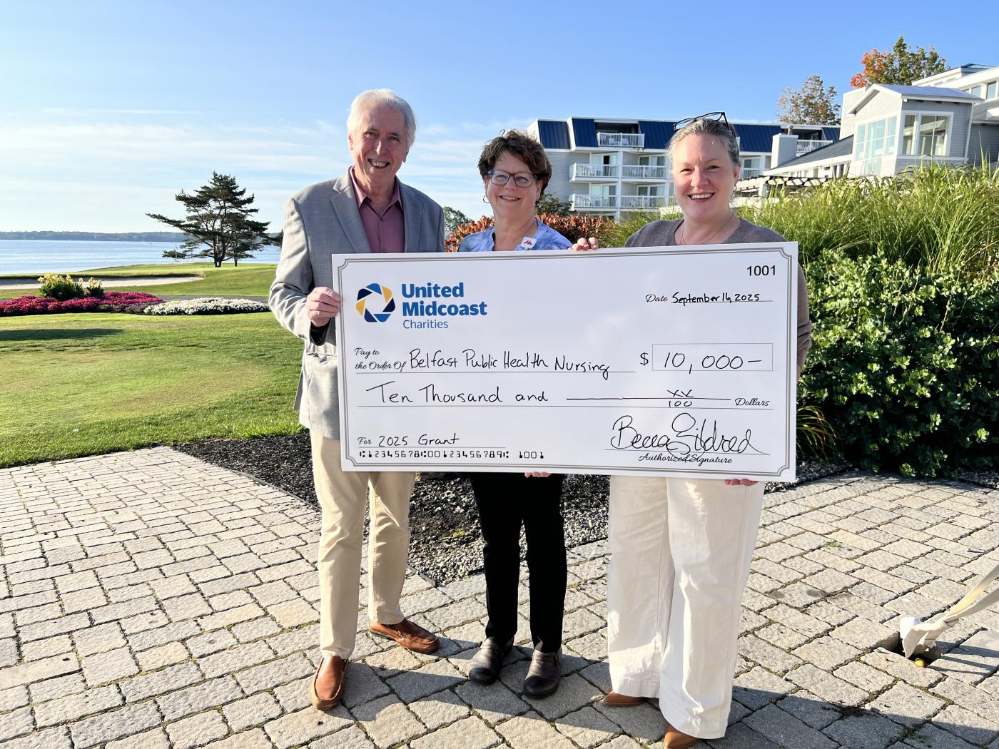 Three adults standing together holding an over-sized check for a grant award presentation
