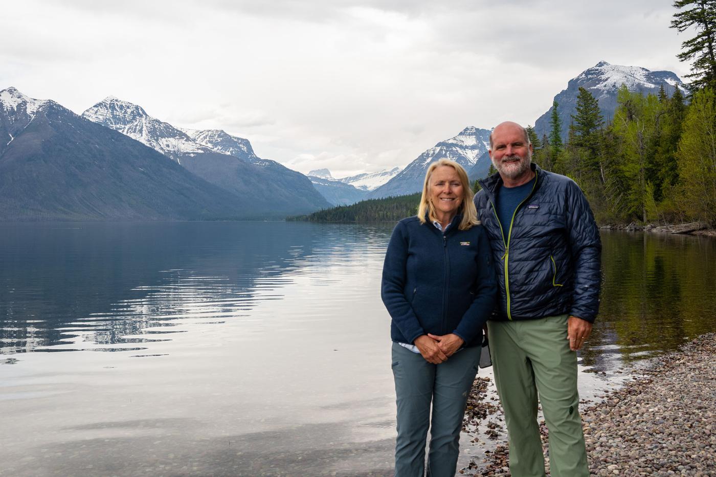 Jeff and Margie Geiger standing together next to a lake with snow-covered mountains behind them