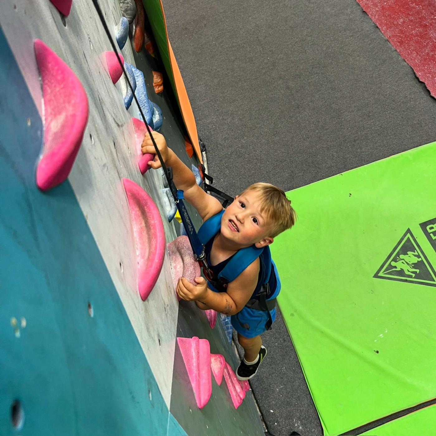A smiling, determined young boy climbing on an indoor rock-climbing wall