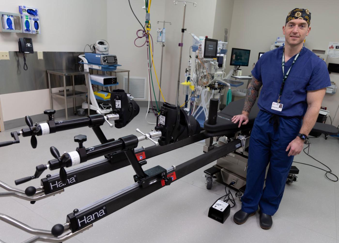 Dr. Zethariah Zielinski wearing scubs and standing next to a specialized orthopedic surgical table in an operating room