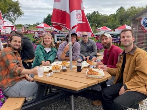 A group of adult sitting around a picnic table outdoors at a restaurant near the ocean