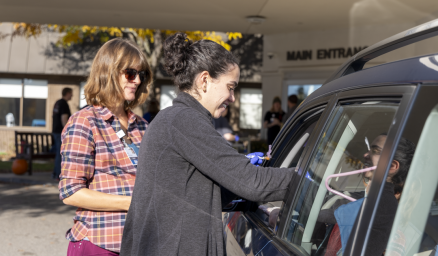 Two care team members administer a flu vaccine to a person through their car window at drive-thru vaccine clinic