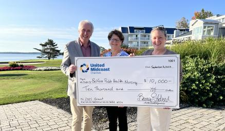 Three adults standing together holding an over-sized check for a grant award presentation