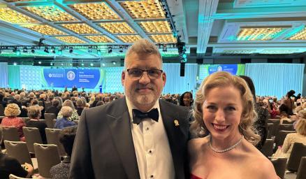 Devin Carr and Valerie Fuller dressed formally and standing together at an awards ceremony in a large room full of people