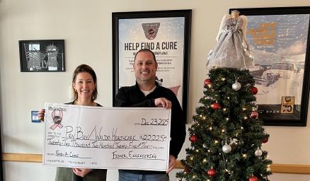 A man and a woman standing together holding an over-sized check for a donation presentation