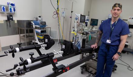 Dr. Zethariah Zielinski wearing scubs and standing next to a specialized orthopedic surgical table in an operating room