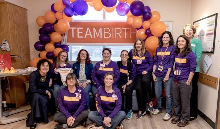 A group of care team members posing together in front of a large balloon arch and banner that says "teambirth"