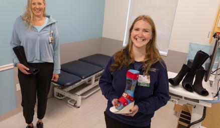 Two care team members in an exam room. They are both holding casting molds for children's foot and leg casts.