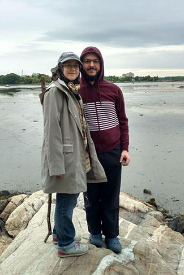 Young man and woman standing together on a rock next to calm water